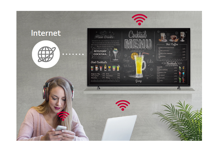 UR640S series is on the wall and a woman is using a personal PC and mobile phone. This image shows that the signage can operate as a virtual router so that the PC and mobile can be connected on the display to get wireless access.