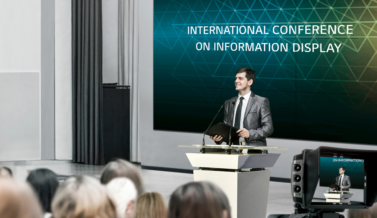 A large video wall is installed in the conference room and a man is holding the conference in front of many people.