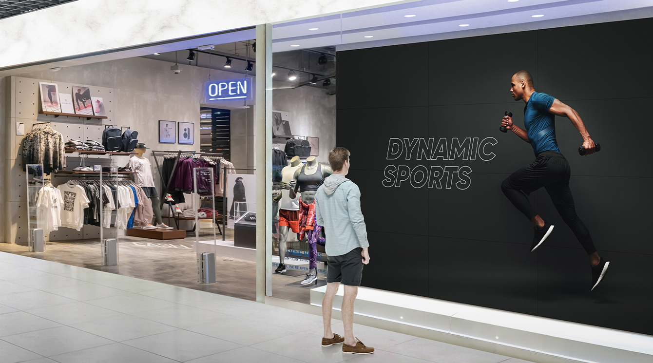 A man is looking at a big screen attached to the window of a sports store.