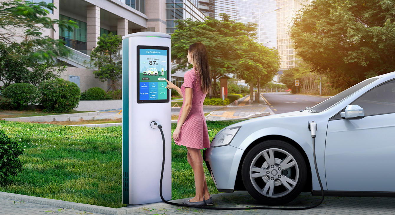A woman is charging a car by touching the touchscreen installed on an electric car charger.
