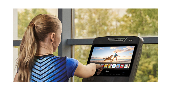 A woman is touching an icon on a TV screen installed on an exercise machine.