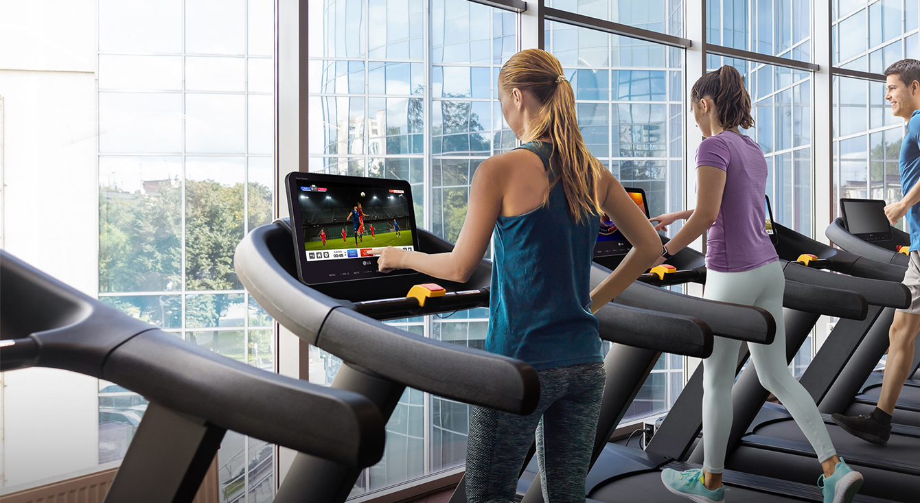 People are running while either touching or watching a running machine’s TV touchscreen lying by the window.