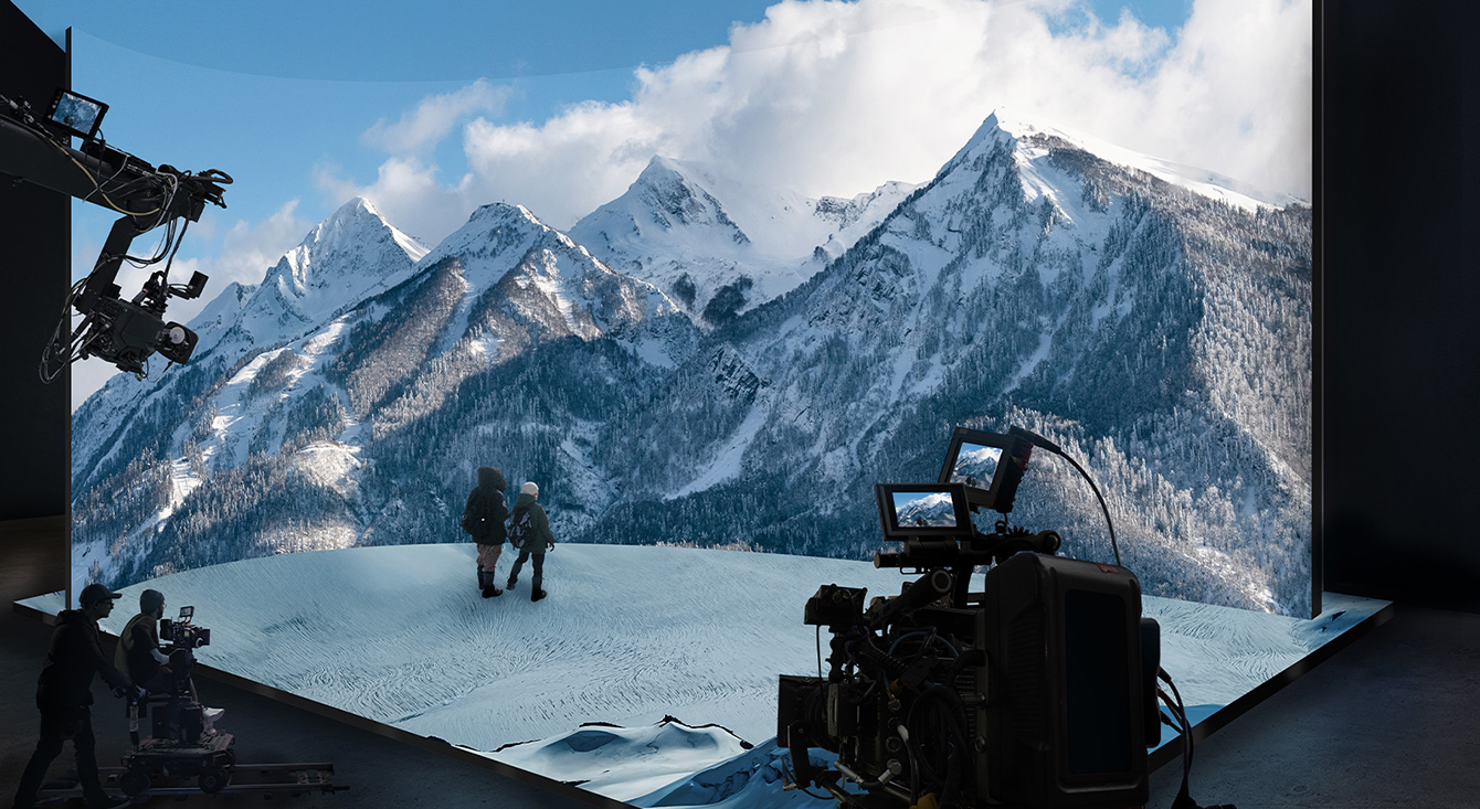 A virtual production studio with curved LED walls and ceiling and floor LEDs is filming a video of snowy mountain scenery.