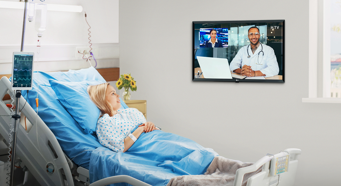 The patient is lying in the hospital room’s bed and watchiccng the TV hanging on the wall.