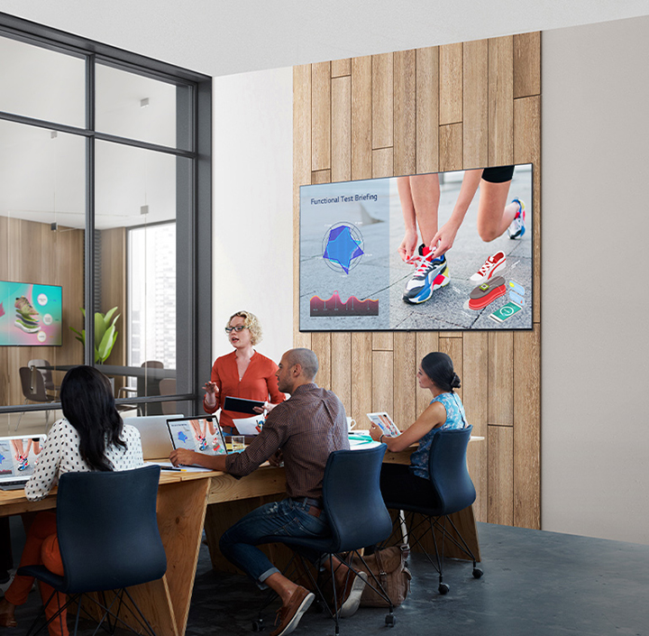There are five people conducting a meeting in a room with UL3J series installed on the wall. There is another UL3J series installed across the meeting room on the wall past the window on the left.
