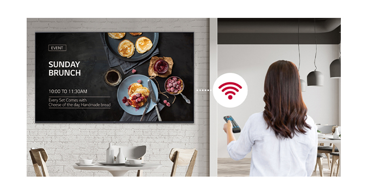 A woman is holding a remote controller and the display is connected in Wi-Fi. The woman is conveniently distributing content or update SW by using a remote controller since the display is connected in network thru Wi-Fi.