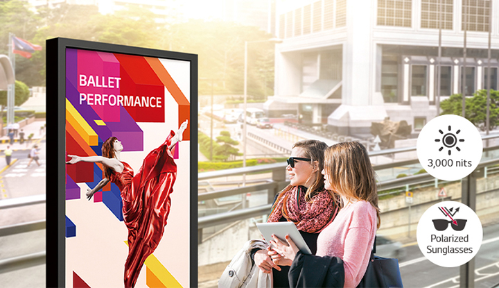 A large-sized display is installed on the street, and women are looking at a vivid-quality advertisement on the screen.