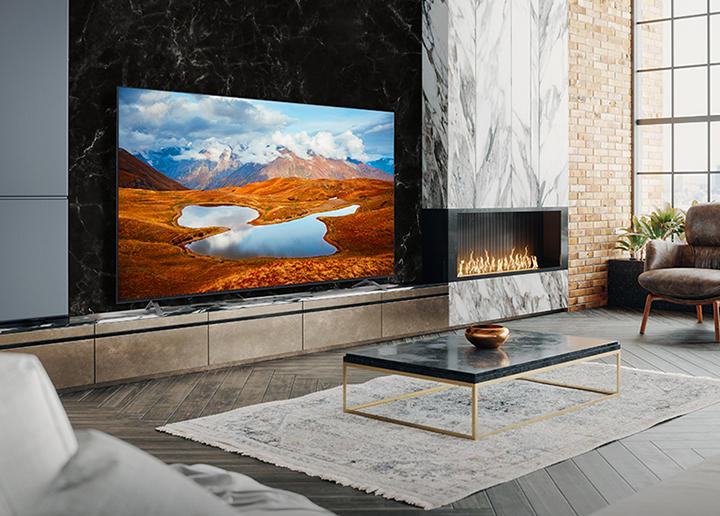 A large TV is placed on a living room wall decorated with a fireplace. Scenery of a mountain at night in which the Milky Way flows is bright and vivid on the TV screen.