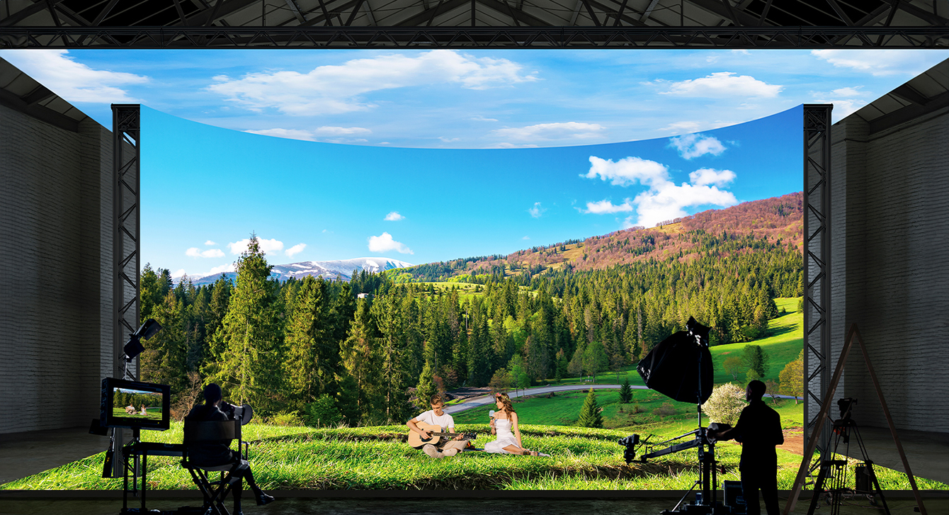 A virtual production studio with curved LED walls and ceiling and floor LEDs is filming images of a forest and field landscape.
