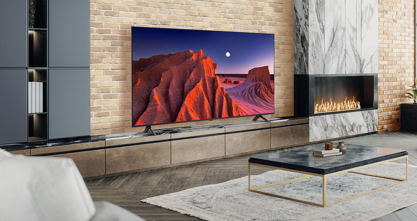 A large TV is placed on a living room wall decorated with a fireplace. The scenery of a mountain at night, with the moon in the sky, is bright and vivid on the TV screen.