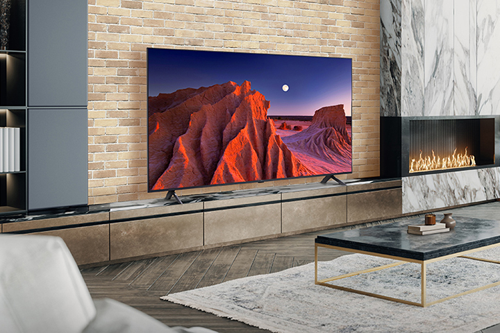 A large TV is placed on a living room wall decorated with a fireplace. The scenery of a mountain at night, with the moon in the sky, is bright and vivid on the TV screen.