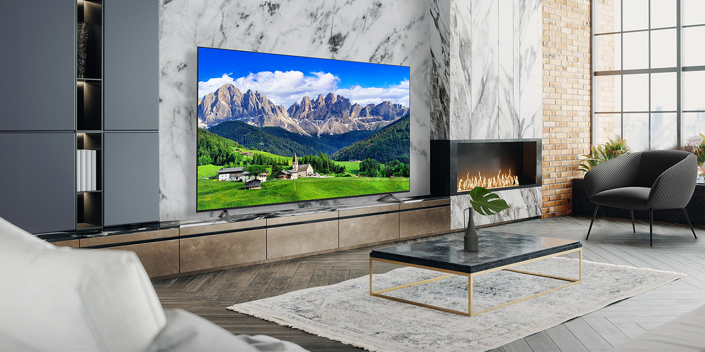 A large TV is placed on a living room wall decorated with a fireplace. The scenery of a mountain and a village is bright and vivid on the TV screen.